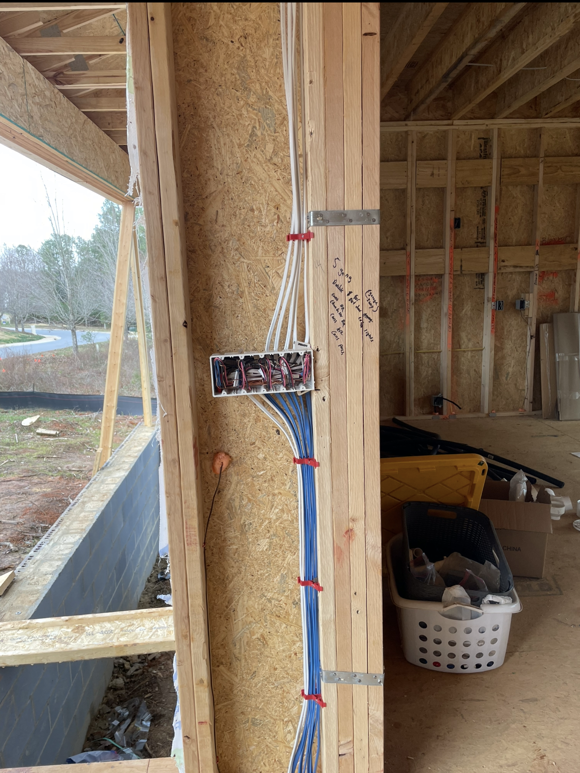 Partially constructed interior wall with exposed electrical wiring, an outlet box, and visible laundry basket in the background—ideal for inspection before adding generator services or completing additional construction work.